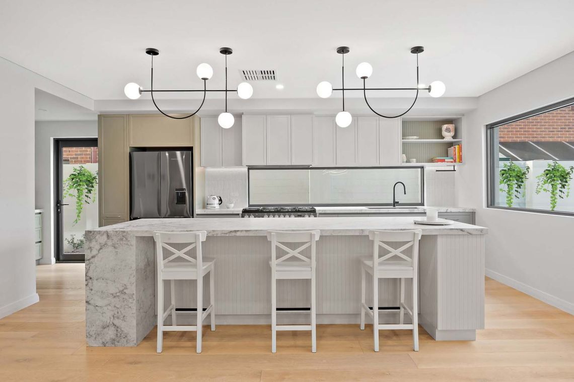 Kitchen with marble waterfall island, cross back stools and globe pendants