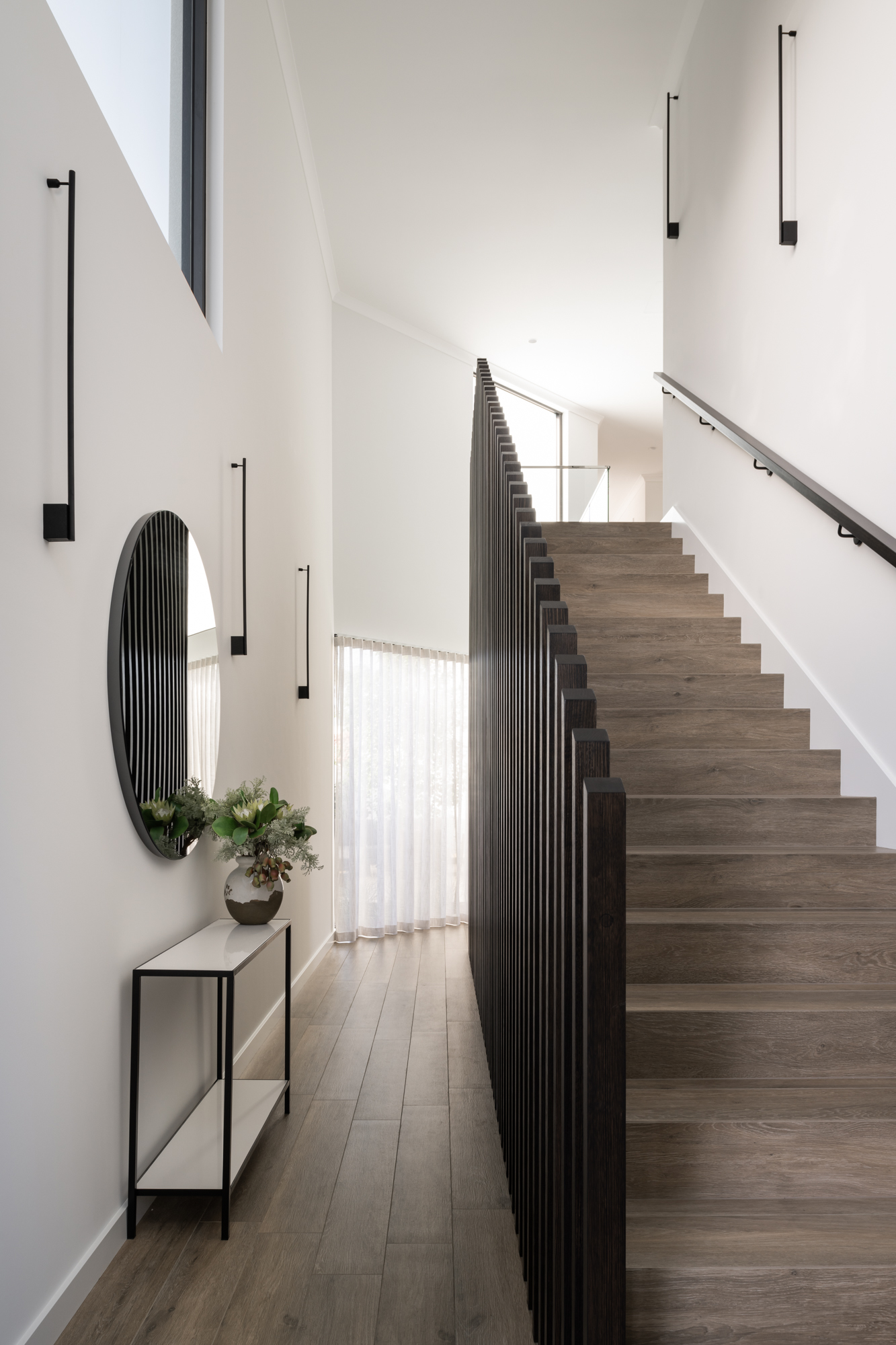 Hallway with timber staircase, slatted balustrade and round mirror in Applecross