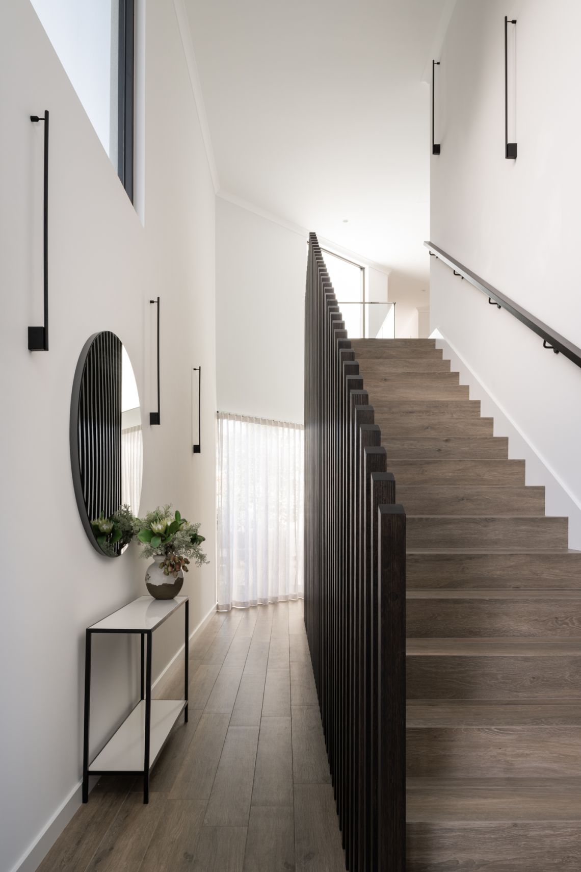 Hallway with timber staircase, slatted balustrade and round mirror in Applecross