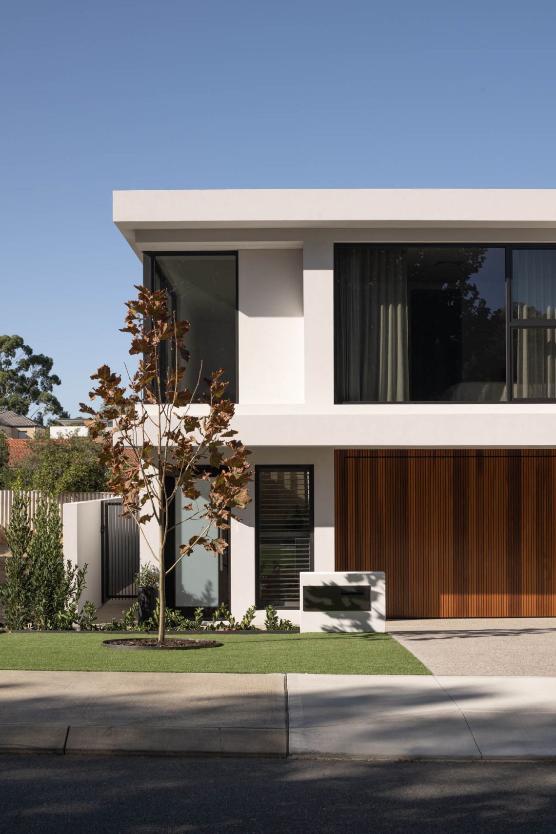 Street view of a two storey home with timber garage door and young tree in Applecross