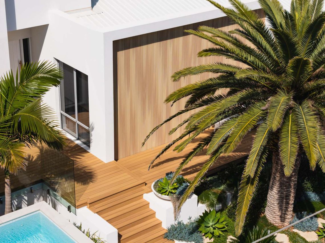 Aerial view of the timber deck, pool and palm at the entry of a City Beach home