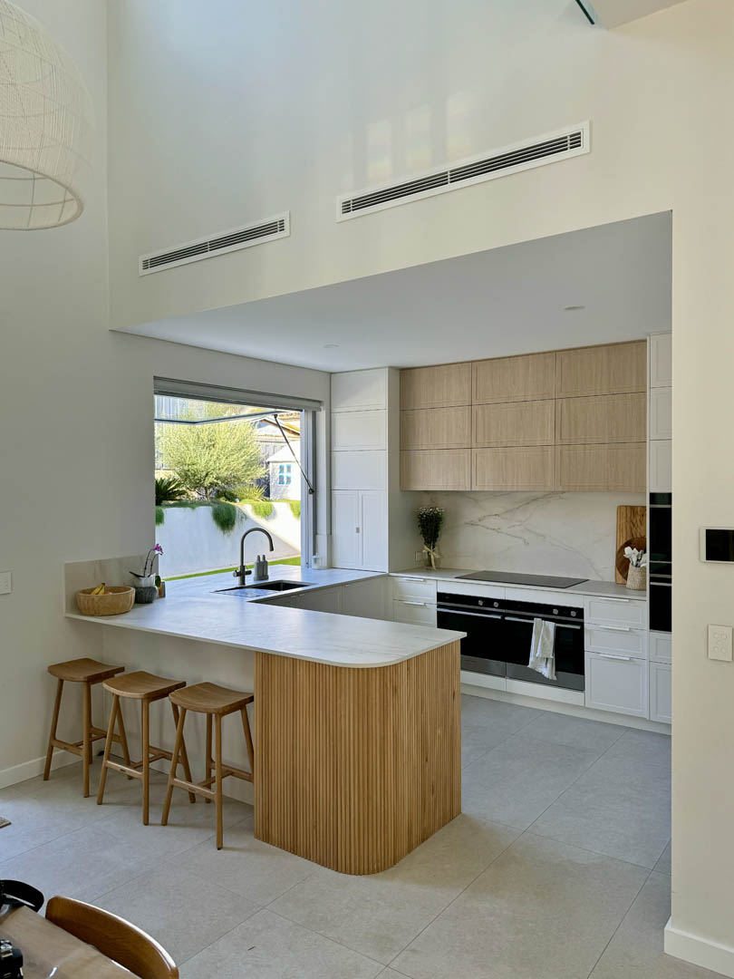 Kitchen under a double height void with fluted timber peninsula in City Beach