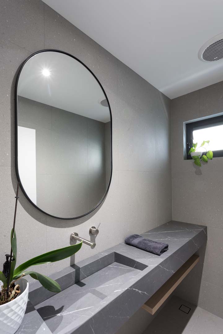 Powder room with stone trough basin and oval mirror in Floreat