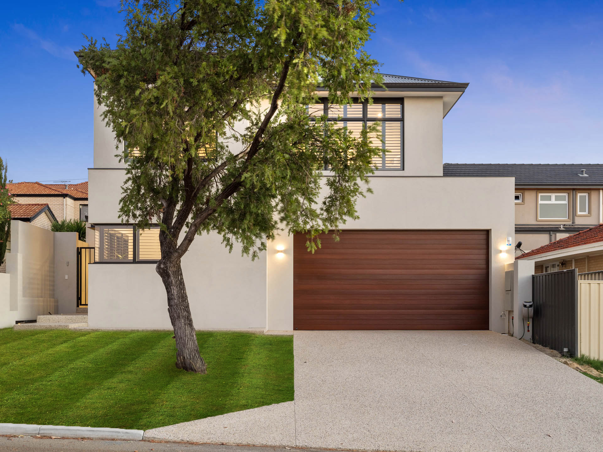 Two storey home with timber garage door and street tree in Tuart Hill